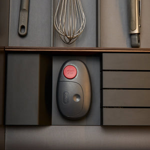 An oval-shaped Zyliss Electronic Can Opener with One-Touch Start/Stop and a red button labeled Start Stop rests in a kitchen drawer organizer alongside other cooking utensils.