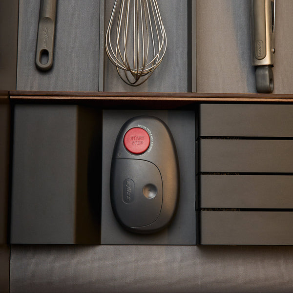 An oval-shaped Zyliss Electronic Can Opener with One-Touch Start/Stop and a red button labeled Start Stop rests in a kitchen drawer organizer alongside other cooking utensils.