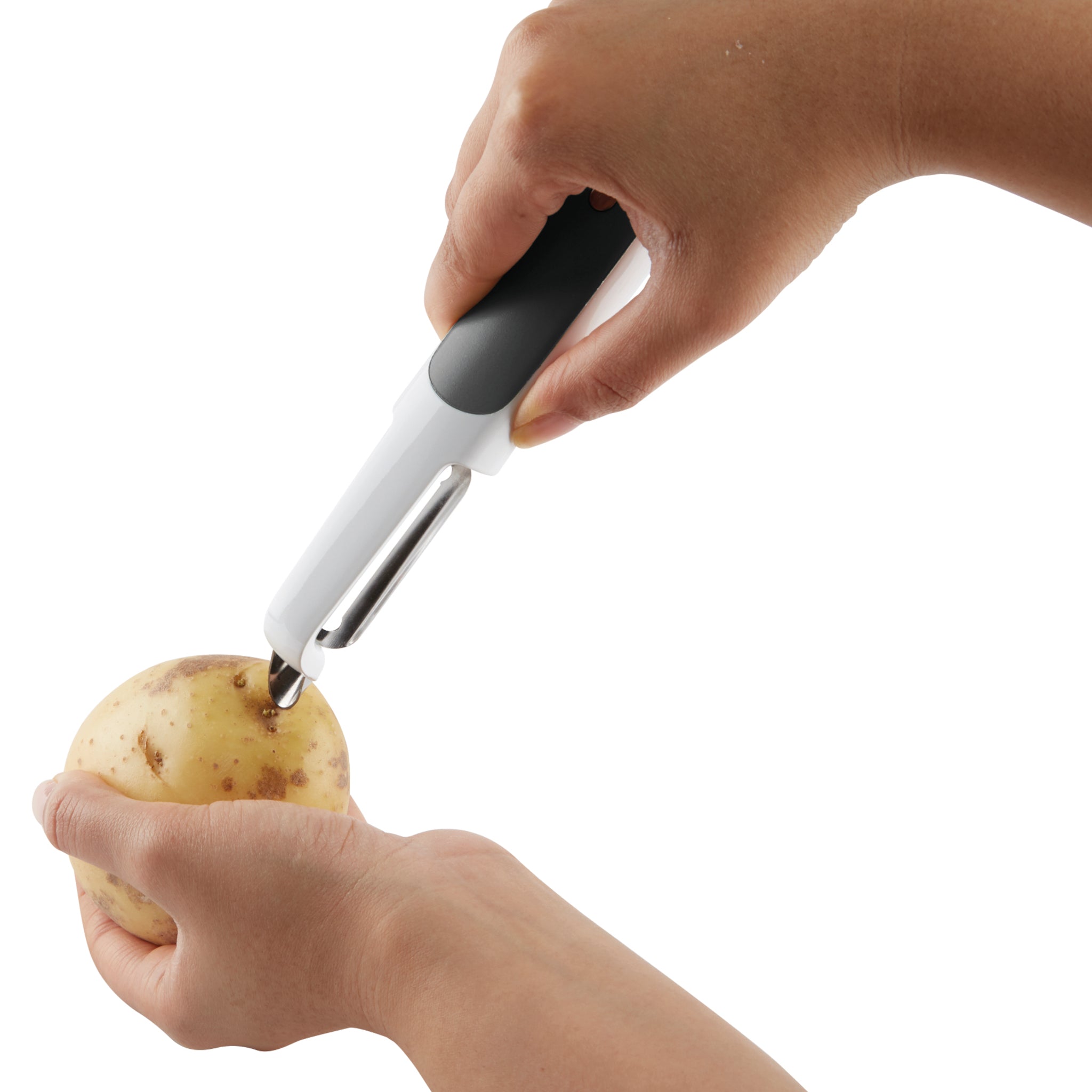 A person uses a black and white vegetable peeler to peel the skin off a potato, holding the potato in one hand and the peeler in the other against a white background.