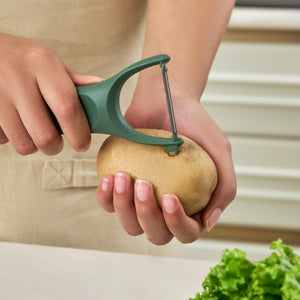 A person peels a potato over a kitchen counter using the Zyliss 3 Piece Y Peeler Set, with fresh lettuce in the foreground.