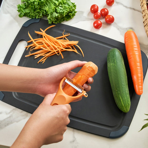Someone uses a Zyliss 3 Piece Y Peeler Set to shred a carrot over a black cutting board with shredded carrot, whole carrot, cucumber, lettuce, and cherry tomatoes nearby.