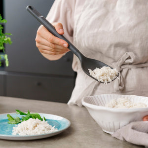 Wearing a light-colored apron, a person uses the Zyliss Spoon to serve cooked white rice from a white bowl onto a blue plate garnished with fresh herbs. #Large