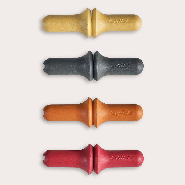 The Zyliss Corn Holders 4 Piece Set features cylindrical holders with ergonomic handles in yellow, black, orange, and red, each with a notch at one end, shown vertically on a light background.