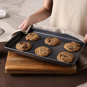 A person holds a tray of cookies fresh from the oven, perfectly baked on the Zyliss Non-Stick Baking Tray for even heat distribution.