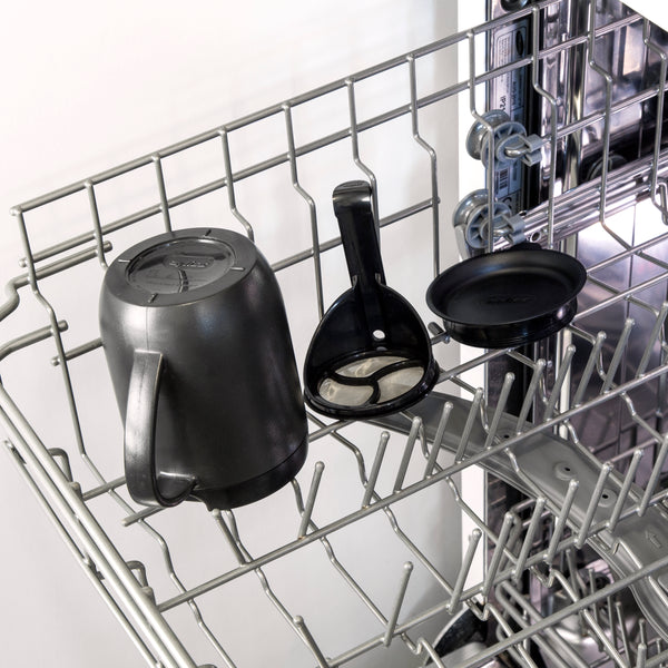 A Zyliss Hot Mug Cafetière Mug, along with its black coffee filter holder and filter lid, sits on the open dishwasher's top rack, ready for cleaning.