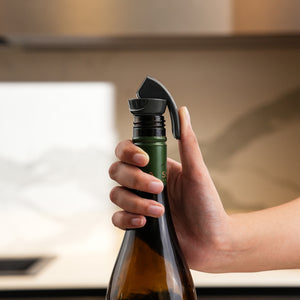 A hand presses a wine bottle onto the Zyliss Bottle Stopper 2 Piece Set in a kitchen, showing efficient drink storage with the black reusable stopper attached to the bottle’s neck.