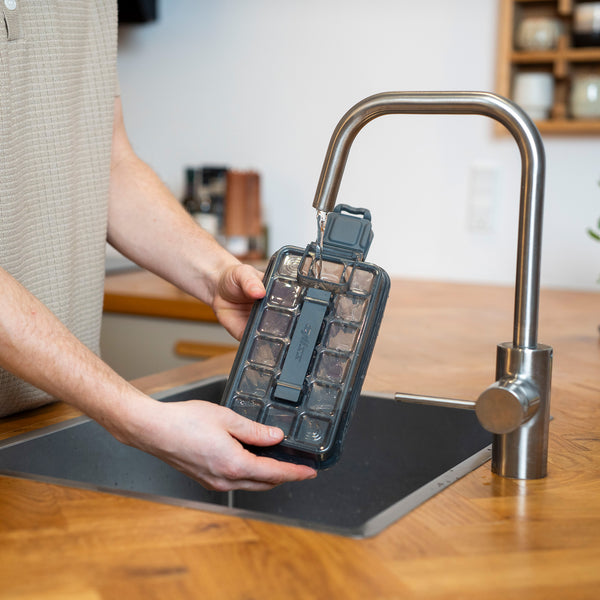 A person holds a Zyliss Press & Pull 2 Piece Ice Cube Tray Set under a kitchen faucet to fill it with water.