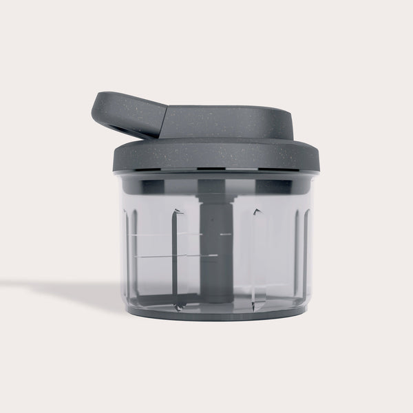 The Zyliss Easy Pull Food Processor features a transparent body, dark gray lid and handle, internal blades, and a modern, minimalist look—this compact manual chopper is set against a plain light background.