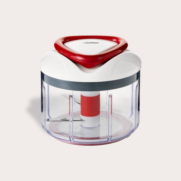 The Zyliss Easy Pull Food Processor is a compact, hand-powered chopper with a clear plastic container, white and red lid, and visible metal blades for easy food prep without electricity. 