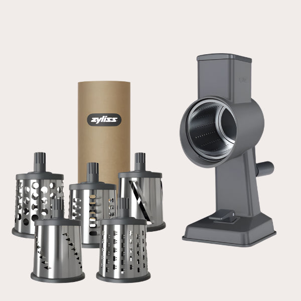The Zyliss Drum Grater & 6 Drum Accessories set, in gray with stainless steel drums and a cylindrical brown storage container, is displayed on a light background—an essential kitchen tool for easy food prep.