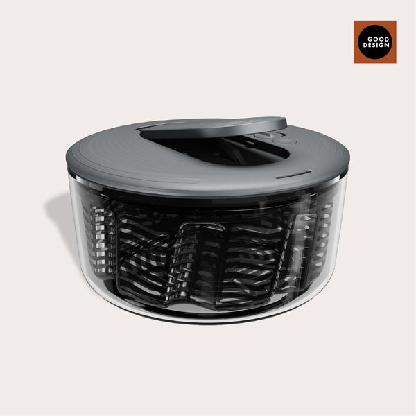 The Zyliss Swift Dry Salad Spinner is a modern, round spinner with a transparent base, dark gray lid, and one-handed pump handle. A GOOD DESIGN award badge is displayed in the upper right corner on a light background.