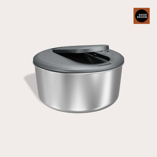 The Zyliss Swift Dry Salad Spinner Stainless Steel features a modern round bowl with a gray textured lid, partially open. A GOOD DESIGN badge appears in the top right on a brown square, highlighting its award-winning style.