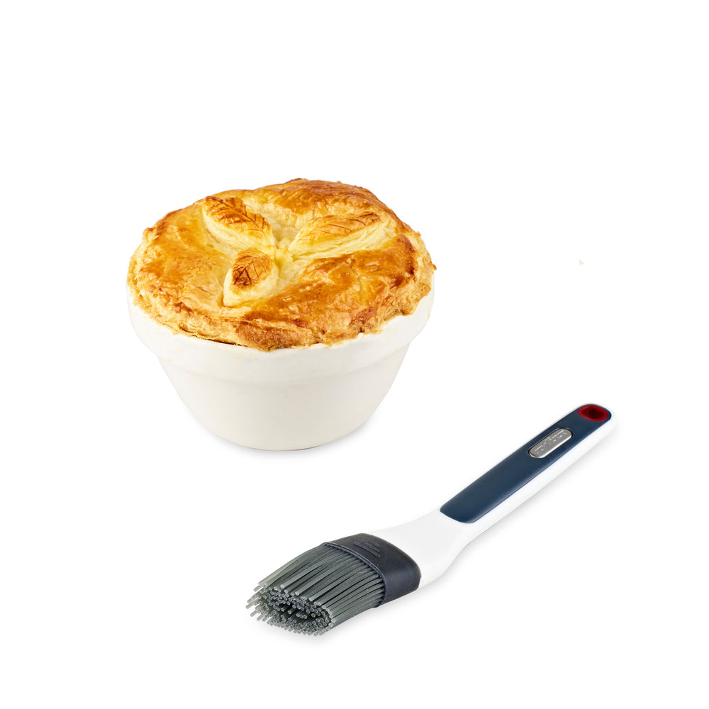 The Zyliss Silicone Pastry Brush, available in black and white, features a long handle with a hanging hole and is dishwasher safe for easy cleaning. 