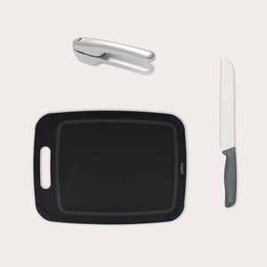 The Zyliss Garlic Bread Making Kit features a black handled cutting board, a silver garlic press, and a gray-handled bread knife—everything you need for garlic bread, elegantly arranged on a light background. #medium