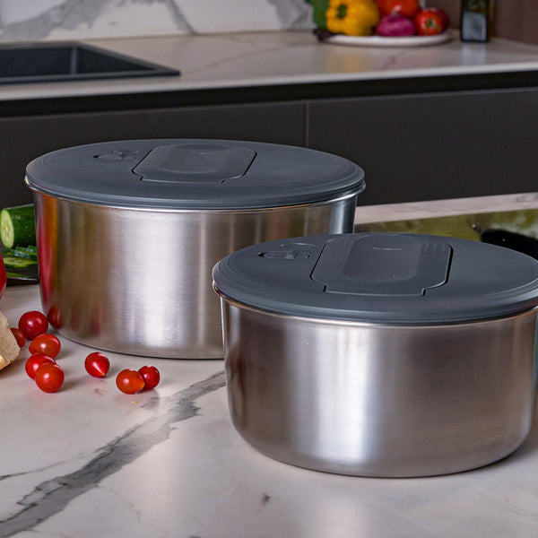 Two Zyliss Swift Dry Salad Spinner Stainless Steel bowls with gray lids rest on a marble countertop, alongside cherry tomatoes, cucumber, and bread—ideal companions for your modern kitchen setup.