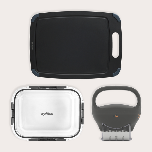 The Zyliss Fresh Prep Kitchen Essentials Set—a black cutting board, a clear-lidded rectangular storage container, and a black handheld slicer—is neatly arranged on a light background, ideal for organized meal prep.