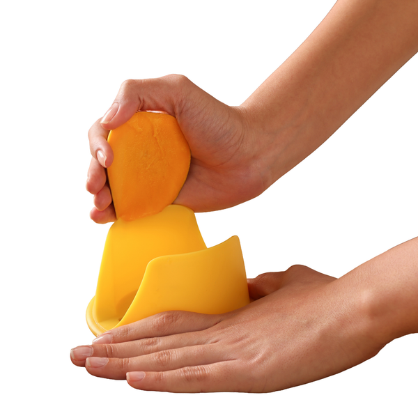 A person uses the Zyliss Mango Splitter, holding the yellow 3-in-1 tool in one hand and pressing half a mango down with the other, slicing it against a white background.