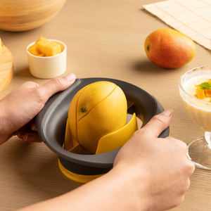 Hands using the Zyliss Mango Splitter to cut a fresh mango on a wooden table, with a whole mango, diced mango, and a dessert garnished with mint in the background.