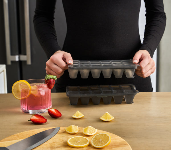 A zyliss Classic Ice Cube Tray held above a second tray beside a drink.