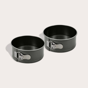 The Zyliss Springform Cake Pan 2 Piece Set, each 20cm/9", features round black non-stick pans with metal latches, shown side by side on a light surface with soft shadows.