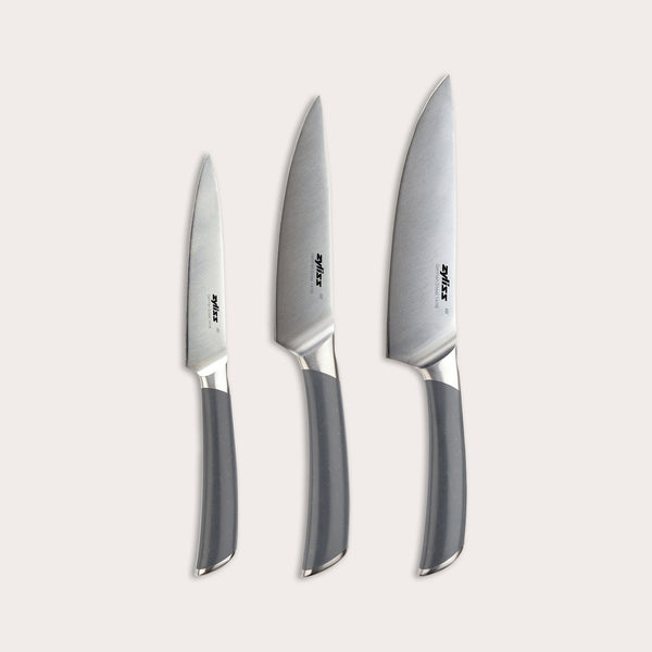 The Zyliss Comfort Pro Prep Trio Knife Set features three kitchen knives—a chef’s knife, a paring knife, and a utility knife—each with silver blades and gray handles, arranged side by side on a light background in order of size from smallest to largest.