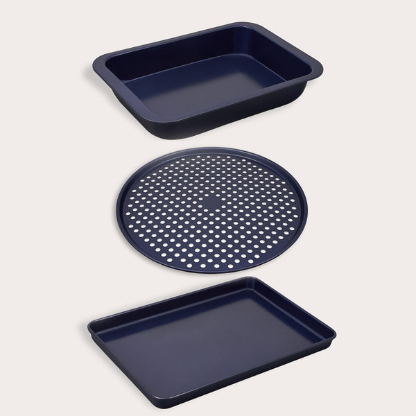 The Zyliss Baking Tray Bundle includes three dark blue carbon steel trays: a deep rectangular non-stick tray, a round perforated pizza pan, and a shallow sheet, all shown on a light background.