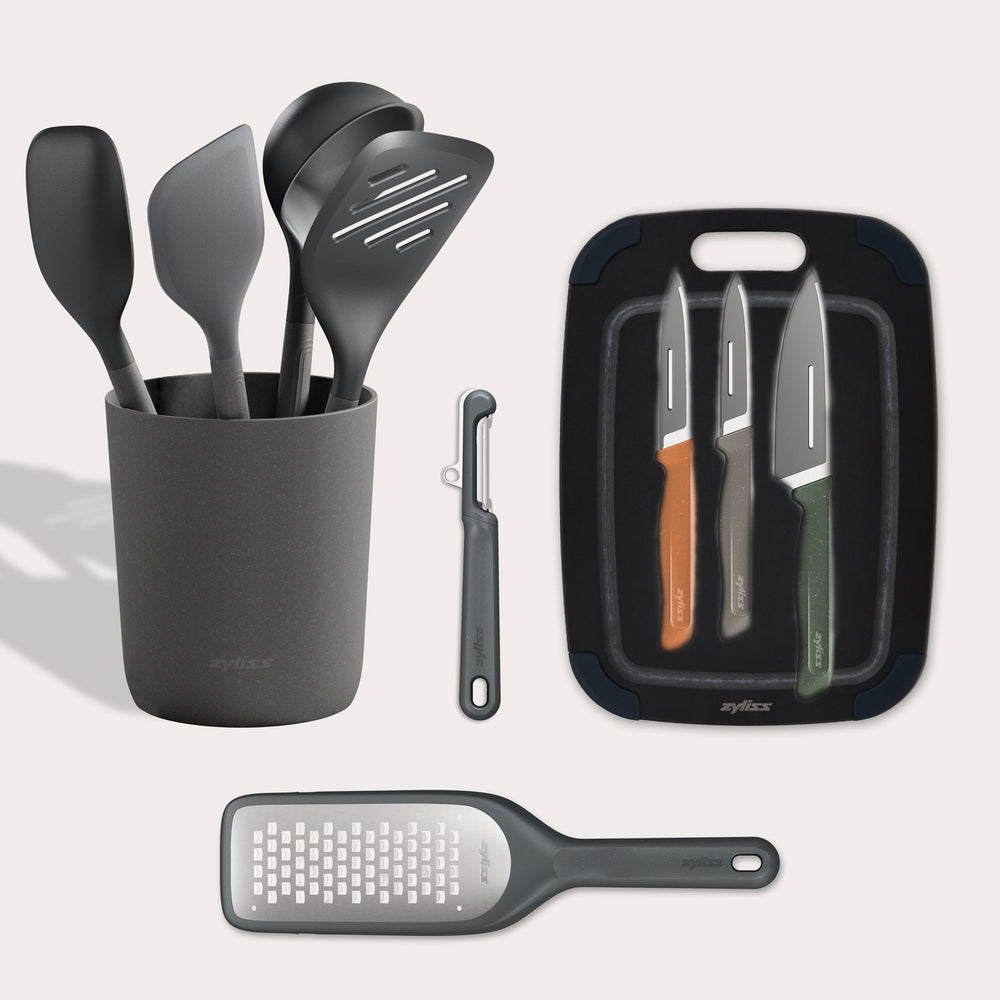 The Zyliss Kitchen Essentials Bundle includes black kitchen tools in a holder, a black peeler, three colorful-handled stainless steel knives with a cutting board, and a flat grater, all displayed on a light background.